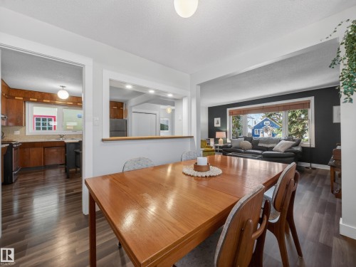 Dining area featuring wood-finish flooring, a pass-through window to the kitchen, and a broad opening to the living space - 11345 89 Street, Edmonton, AB - Indoor Photo Showing Dining Room