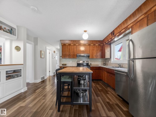 Kitchen featuring wood-finish cabinetry, stainless steel appliances, solid surface countertops, and wood-finish flooring - 11345 89 Street, Edmonton, AB - Indoor Photo Showing Kitchen With Double Sink