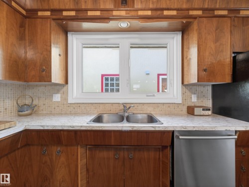 Kitchen workstation featuring a double basin stainless steel sink, wood-finish cabinetry, and a mosaic tile backsplash - 11345 89 Street, Edmonton, AB - Indoor Photo Showing Kitchen With Double Sink