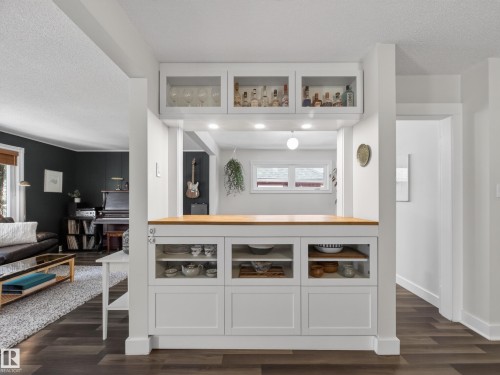 Built-in bar area featuring a light wood countertop, recessed lighting, and upper cabinetry with glass-front doors - 11345 89 Street, Edmonton, AB - Indoor