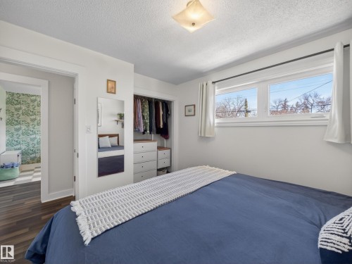 Bright room featuring wood-finish flooring, two large windows, a built-in closet system with drawers, and an entryway to an additional space with patterned wallpaper - 11345 89 Street, Edmonton, AB - Indoor Photo Showing Bedroom