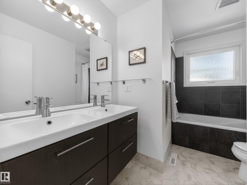 Modern bathroom featuring a dual-sink vanity with dark wood-finish cabinetry, chrome fixtures, a large mirror, and hexagonal floor tiling - 11345 89 Street, Edmonton, AB - Indoor Photo Showing Bathroom