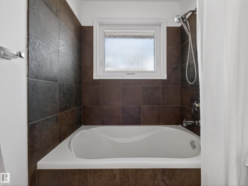 Built-in bathtub with an integrated shower fixture, brown tile surround, and a white framed window with textured glass - 11345 89 Street, Edmonton, AB - Indoor Photo Showing Bathroom