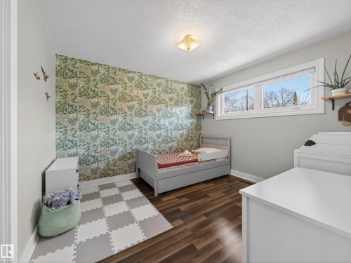 Room featuring a decorative accent wall, wood-finish flooring, and white trim - 11345 89 Street, Edmonton, AB - Indoor