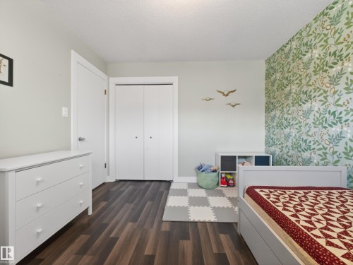 Bedroom featuring wood-finish flooring, a patterned accent wall, and a white bi-fold closet - 11345 89 Street, Edmonton, AB - Indoor Photo Showing Bedroom