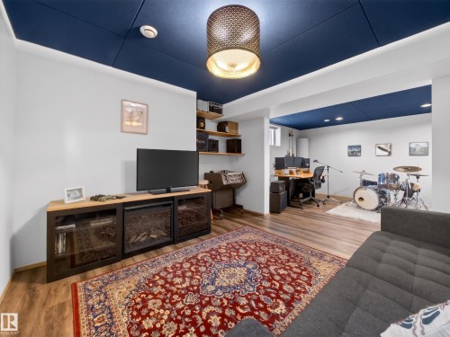 Entertainment area featuring wood-finish flooring, a built-in media console with an electric fireplace, and a deep blue acoustic panel ceiling - 11345 89 Street, Edmonton, AB - Indoor
