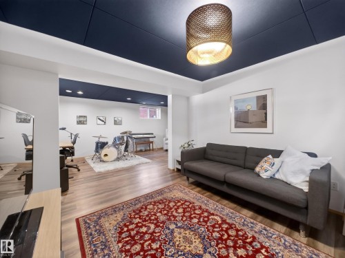 Spacious recreation room featuring wood-finish flooring, a dark blue ceiling with recessed lighting, and a distinctive gold-tone drum pendant light - 11345 89 Street, Edmonton, AB - Indoor Photo Showing Living Room