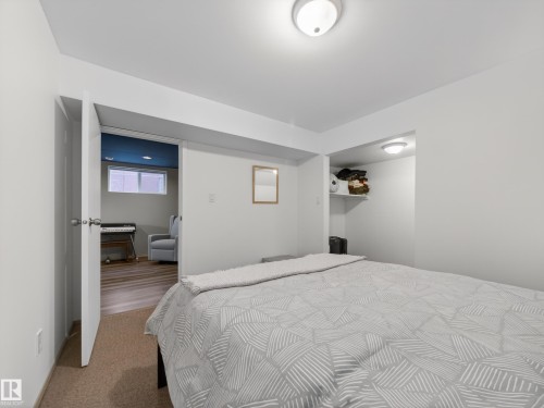 Carpeted room with recessed shelving, an integrated ceiling light fixture, and a doorway opening to a room with wood-finish flooring - 11345 89 Street, Edmonton, AB - Indoor Photo Showing Bedroom