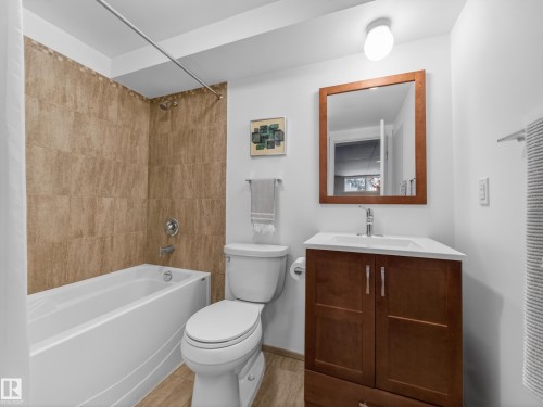 Bathroom featuring a tub/shower combination with tile surround, a single vanity with a white countertop, and wood-finish flooring - 11345 89 Street, Edmonton, AB - Indoor Photo Showing Bathroom