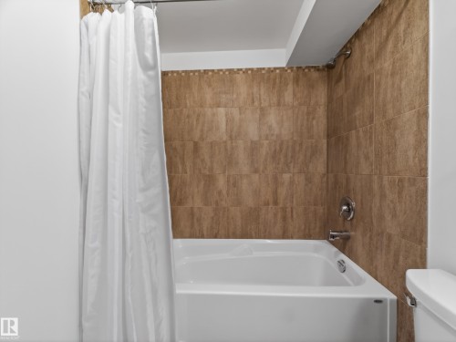 White bathtub with chrome fixtures, surrounded by textured brown wall tile and a decorative mosaic border - 11345 89 Street, Edmonton, AB - Indoor Photo Showing Bathroom