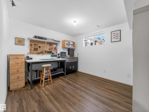 Spacious room featuring wood-finish flooring, a functional workbench, pegboard organization, an overhead track light, and a window providing natural illumination - 11345 89 Street, Edmonton, AB - Indoor