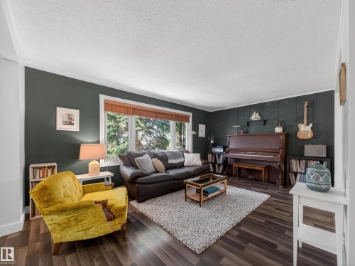 Living area featuring wood-finish flooring, a large picture window with wood blinds, and dark accent walls with white trim - 11345 89 Street, Edmonton, AB - Indoor Photo Showing Living Room
