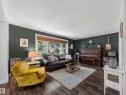 Living area featuring wood-finish flooring, a large picture window with wood blinds, and dark accent walls with white trim - 11345 89 Street, Edmonton, AB  - Indoor Photo Showing Living Room 