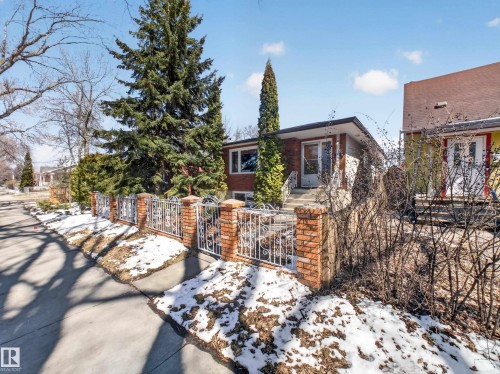 Brick exterior featuring a white entry door, elevated entryway with white railings, and mature evergreen trees - 11345 89 Street, Edmonton, AB - Outdoor