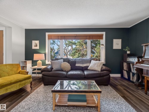 Expansive window with wood-finish blinds, dark accent wall, crown molding, and wood-finish flooring - 11345 89 Street, Edmonton, AB - Indoor Photo Showing Living Room