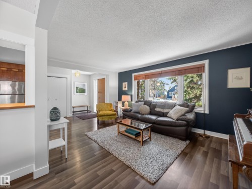Spacious living area featuring dark wood-finish flooring, a large picture window with wood blinds, and a built-in pass-through window to the kitchen - 11345 89 Street, Edmonton, AB - Indoor Photo Showing Living Room