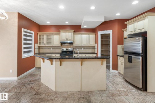Kitchen featuring a central island with a dark granite countertop, light-toned cabinetry, stainless steel appliances, and a tile backsplash - 3455 29 Street, Edmonton, AB - Indoor Photo Showing Kitchen