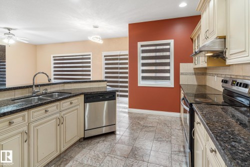 Kitchen featuring granite countertops, stainless steel appliances, cream cabinetry, a double basin sink with gooseneck faucet, and tile flooring - 3455 29 Street, Edmonton, AB - Indoor Photo Showing Kitchen With Double Sink