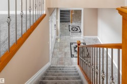 Split-level foyer featuring gray floor tiles with a black and white geometric inlay, a light wood-finish staircase railing, and wrought iron balusters - 
