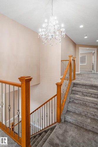 Stairwell featuring a multi-tiered crystal chandelier, wood handrails, wrought iron balusters, and carpeted stairs - 3455 29 Street, Edmonton, AB - Indoor Photo Showing Other Room