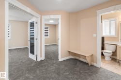 Hallway area featuring plush gray carpet, a built-in bench, and entryways to two carpeted rooms and a bathroom - 