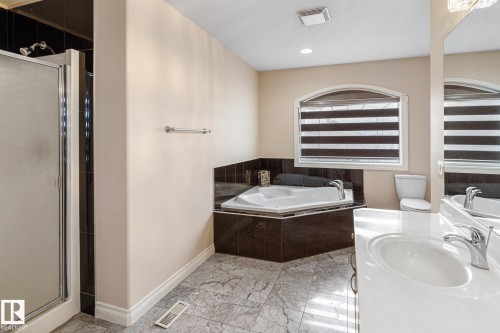 Bathroom featuring a corner jetted tub, a separate glass-enclosed shower, a vanity with a white countertop and integrated sink, chrome fixtures, and patterned floor tiling - 3455 29 Street, Edmonton, AB - Indoor Photo Showing Bathroom
