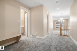 Upper-level hallway featuring plush gray carpeting, neutral wall tones, white trim, and a built-in bench - 