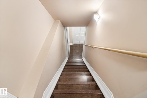 Stairwell featuring wood-finish treads, light-toned wall paint, white baseboards, a natural wood handrail, and a wall-mounted light fixture - 3455 29 Street, Edmonton, AB - Indoor Photo Showing Other Room
