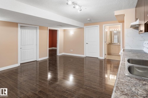 Open concept room featuring wood-finish flooring, light peach walls, white trim, and a textured ceiling - 3455 29 Street, Edmonton, AB - Indoor Photo Showing Kitchen With Double Sink