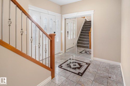 Foyer featuring tiled flooring with a decorative inlay, a wood and wrought iron staircase, double entry doors with decorative glass inserts, and a mirrored closet - 3455 29 Street, Edmonton, AB - Indoor Photo Showing Other Room