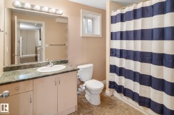 Bathroom featuring a single vanity with a white basin and a speckled countertop, a toilet, a full-size mirror with strip lighting, and a shower with a shower curtain - 