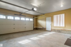 Attached garage featuring a white overhead door with upper window inserts, a side entry door, and a window with vertical blinds - 