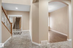 Foyer featuring light-toned tile flooring, a wood staircase with decorative iron spindles, and a mirrored closet - 