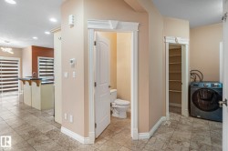 Tiled flooring extends through this area, featuring a powder room with a pedestal toilet, a laundry area with a built-in washing machine, and an adjacent pantry with integrated shelving - 
