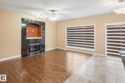 Spacious interior featuring a dark stone fireplace with an arched niche, wood-finish flooring, large windows with horizontal blinds, and a ceiling fan - 