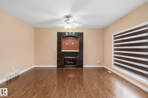 Spacious living area featuring wood-finish flooring, a built-in fireplace with a dark stone surround and arched alcove, a ceiling fan, and a large window with horizontal blinds - 3455 29 Street, Edmonton, AB - Indoor With Fireplace