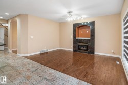 Living area featuring hardwood flooring, a gas fireplace with a dark stone surround and arched niche, and a ceiling fan with integrated lighting - 
