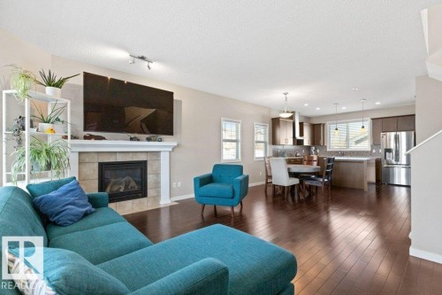 Spacious living area featuring wood-finish flooring, a tiled fireplace with white mantle, and track lighting - 575 Allard Boulevard, Edmonton, AB - Indoor Photo Showing Living Room With Fireplace