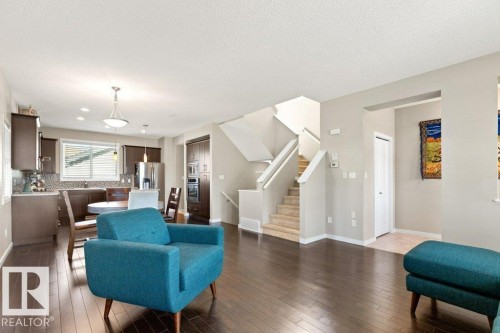 Expansive open-concept living area featuring dark wood-finish flooring, a contemporary kitchen with stainless steel appliances, a breakfast bar, and a dedicated dining space under a pendant light - 575 Allard Boulevard, Edmonton, AB - Indoor Photo Showing Living Room