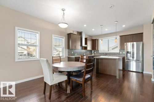 Open-concept kitchen and dining area featuring dark wood-finish flooring, a tiled backsplash, stainless steel appliances, recessed lighting, and pendant lighting fixtures - 575 Allard Boulevard, Edmonton, AB - Indoor