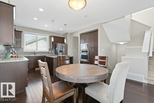 Kitchen and dining area featuring wood-finish flooring, dark wood cabinetry, a mosaic tile backsplash, and a built-in oven and microwave - 575 Allard Boulevard, Edmonton, AB - Indoor Photo Showing Dining Room