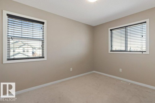 Neutral-toned room featuring two windows with white trim, dark blinds, and light-colored carpet flooring - 575 Allard Boulevard, Edmonton, AB - Indoor Photo Showing Other Room