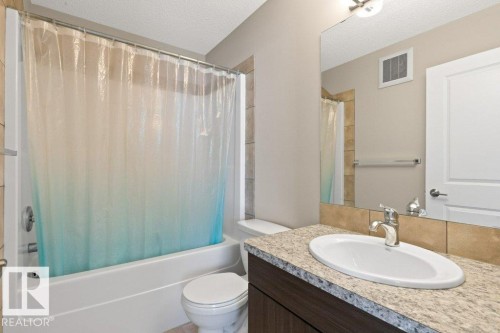 Bathroom featuring a white bathtub with a tile surround, a toilet, a vanity with a light-colored countertop, an oval undermount sink, and a chrome faucet - 575 Allard Boulevard, Edmonton, AB - Indoor Photo Showing Bathroom