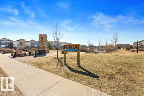 Manicured green space featuring a paved pathway, decorative stone columns, and a pond with surrounding landscaping - 575 Allard Boulevard, Edmonton, AB - Outdoor With View