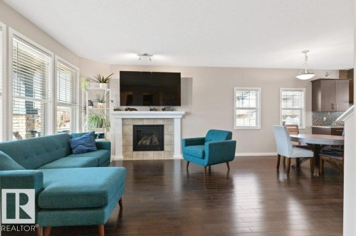 Spacious living area featuring wood-finish flooring, a tiled fireplace with a white mantel, and ample natural light from multiple windows - 575 Allard Boulevard, Edmonton, AB - Indoor Photo Showing Living Room With Fireplace