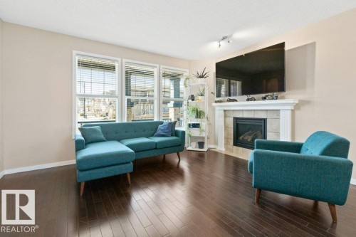 Living area with dark wood-finish flooring, a fireplace featuring a tile surround and white mantel, and track lighting - 575 Allard Boulevard, Edmonton, AB - Indoor Photo Showing Living Room With Fireplace