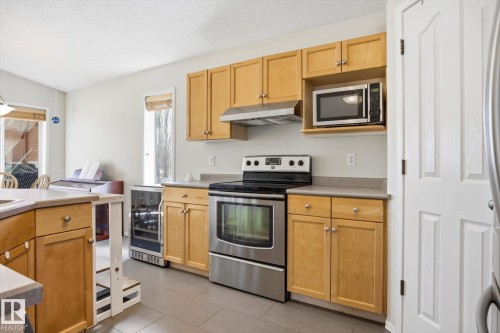 Kitchen featuring natural wood-finish cabinetry, stainless steel range and microwave, and a built-in wine refrigerator - 2251 Brennan Court, Edmonton, AB - Indoor Photo Showing Kitchen With Stainless Steel Kitchen