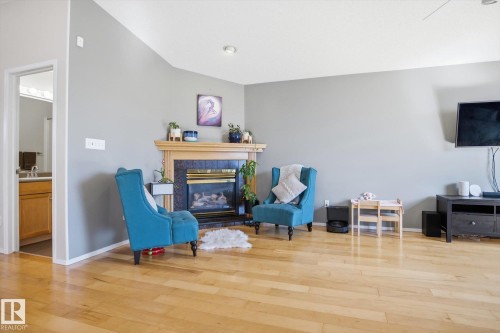 Living area featuring light wood-finish flooring, a corner fireplace with a black stone surround and wood mantel, and vaulted ceilings - 2251 Brennan Court, Edmonton, AB - Indoor With Fireplace