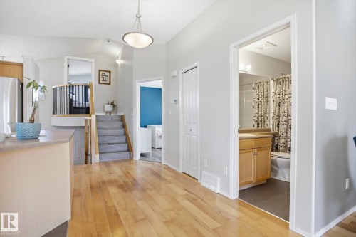 Open-concept living space featuring wood-finish flooring, vaulted ceilings, and a staircase with carpeted treads and a black metal spindle railing - 2251 Brennan Court, Edmonton, AB - Indoor