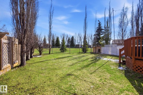 Expansive backyard featuring a lush green lawn, mature trees, a wood privacy fence with lattice accents, a white lattice fence, and a multi-level wood deck with railings - 2251 Brennan Court, Edmonton, AB - Outdoor